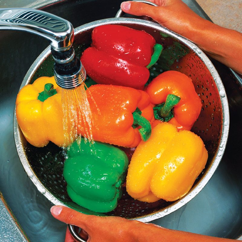 Fresh peppers being rinsed under a kitchen tap